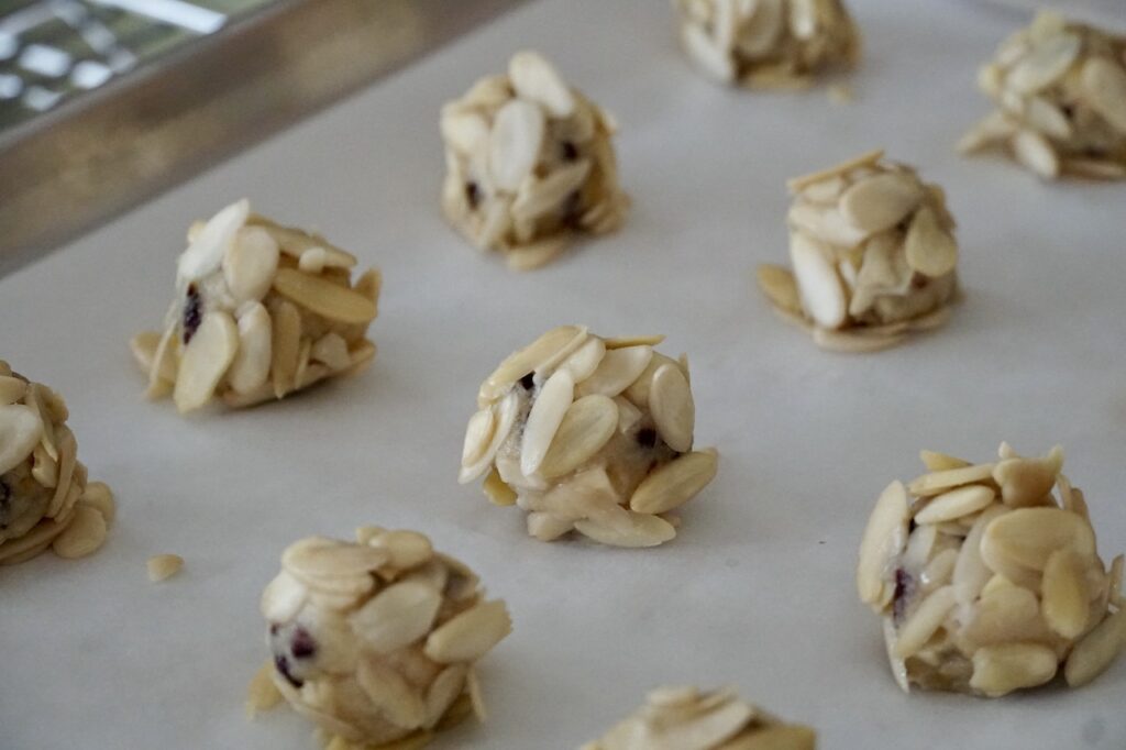 The cookie balls rolled in egg whites and almond slices, placed onto a baking sheet.