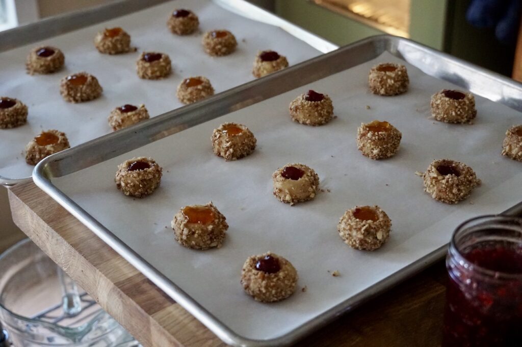 The thumbprint cookies topped with a dollop of jam, lined up on a baking tray.