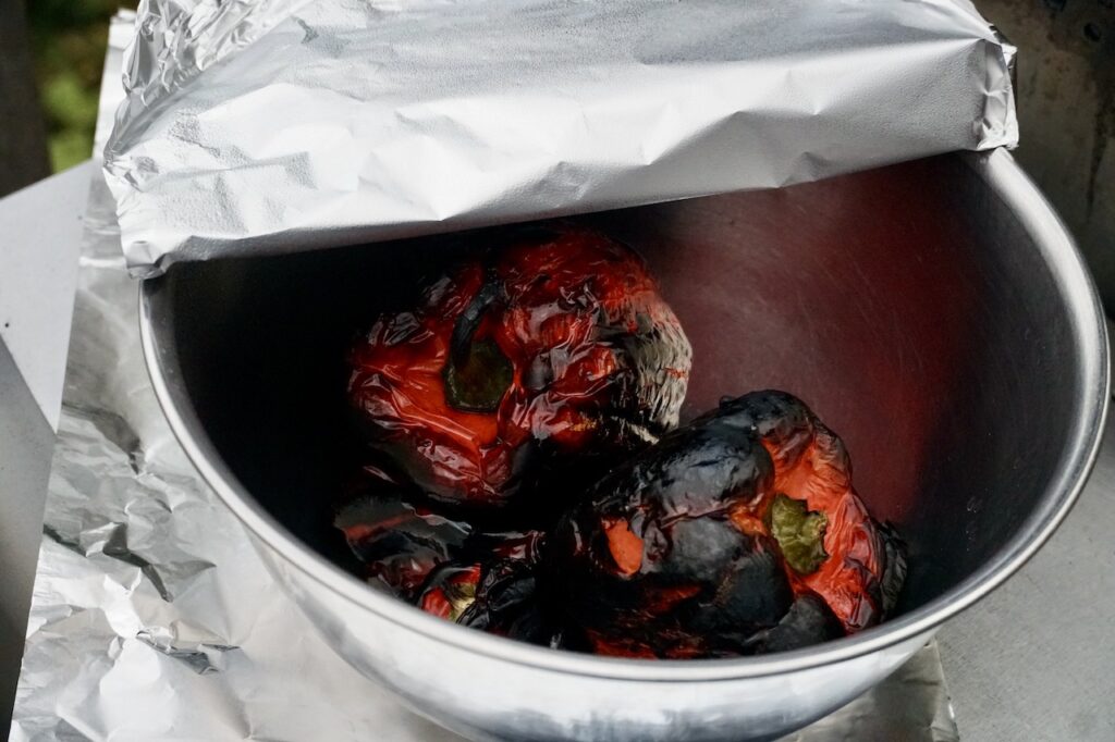 The grilled peppers placed in a bowl, covered with foil.