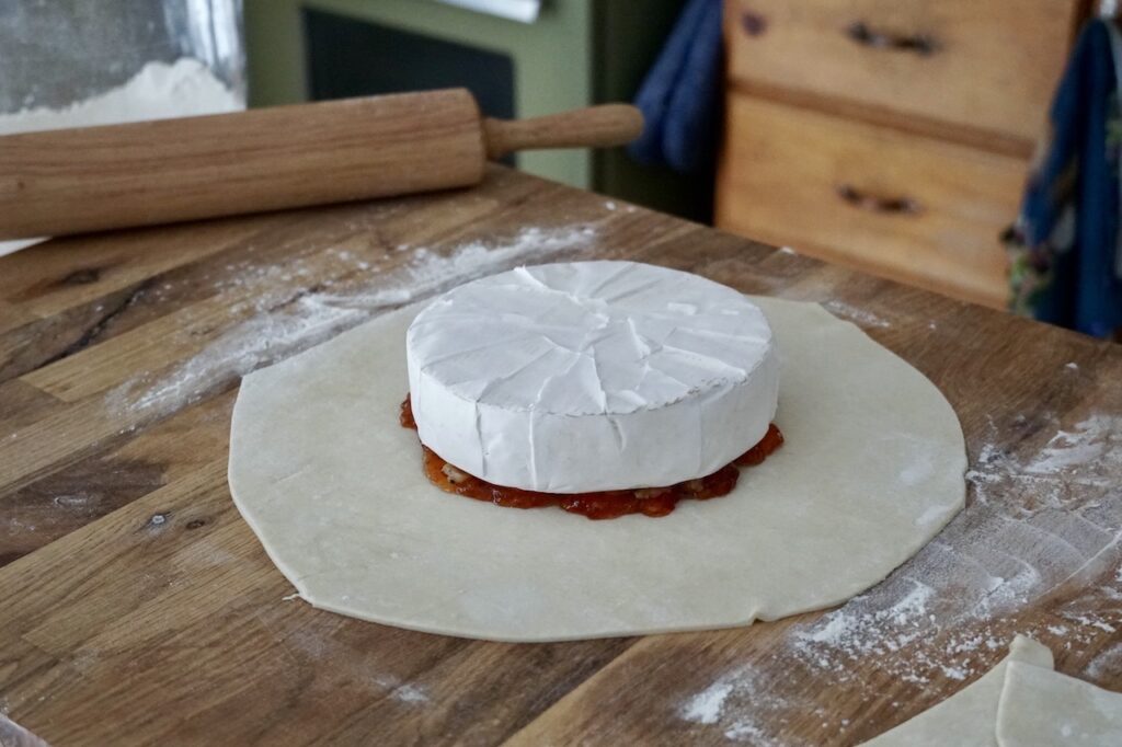 The wheel of brie resting on the jelly and pear mixture in the centre of the sheet of puff pastry.