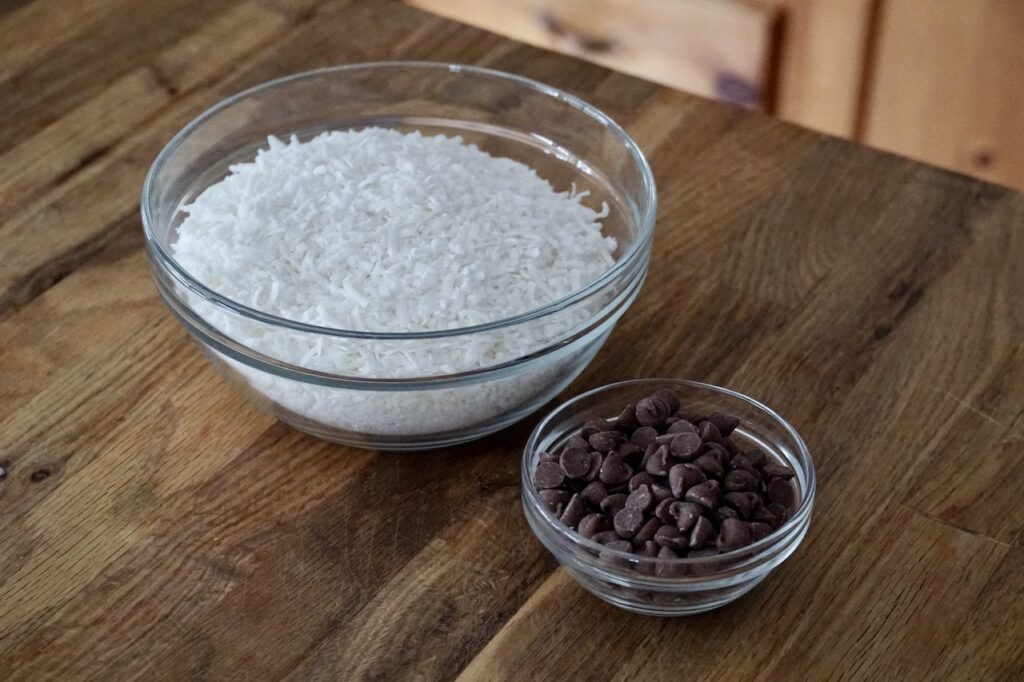 A bowl of sweetened shredded coconut and a bowl of milk chocolate chips.