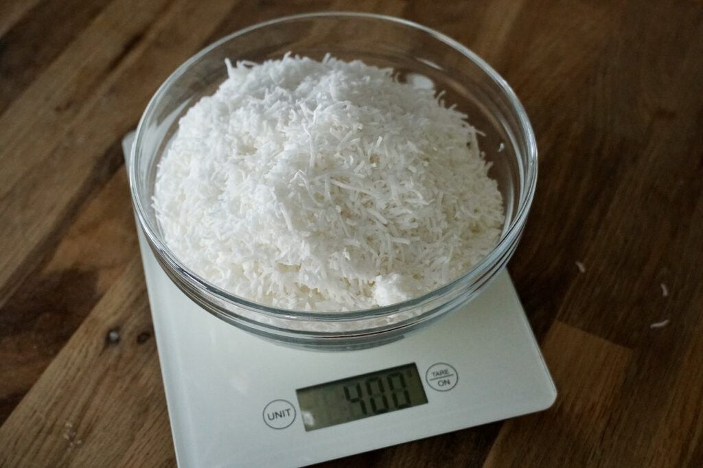 A bowl of shredded coconut in a bowl resting on a kitchen scale.