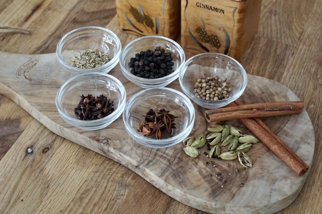 Bowls containing fennel seeds, black peppercorns, coriander, cloves, star anise, cinnamon sticks and cardamom.