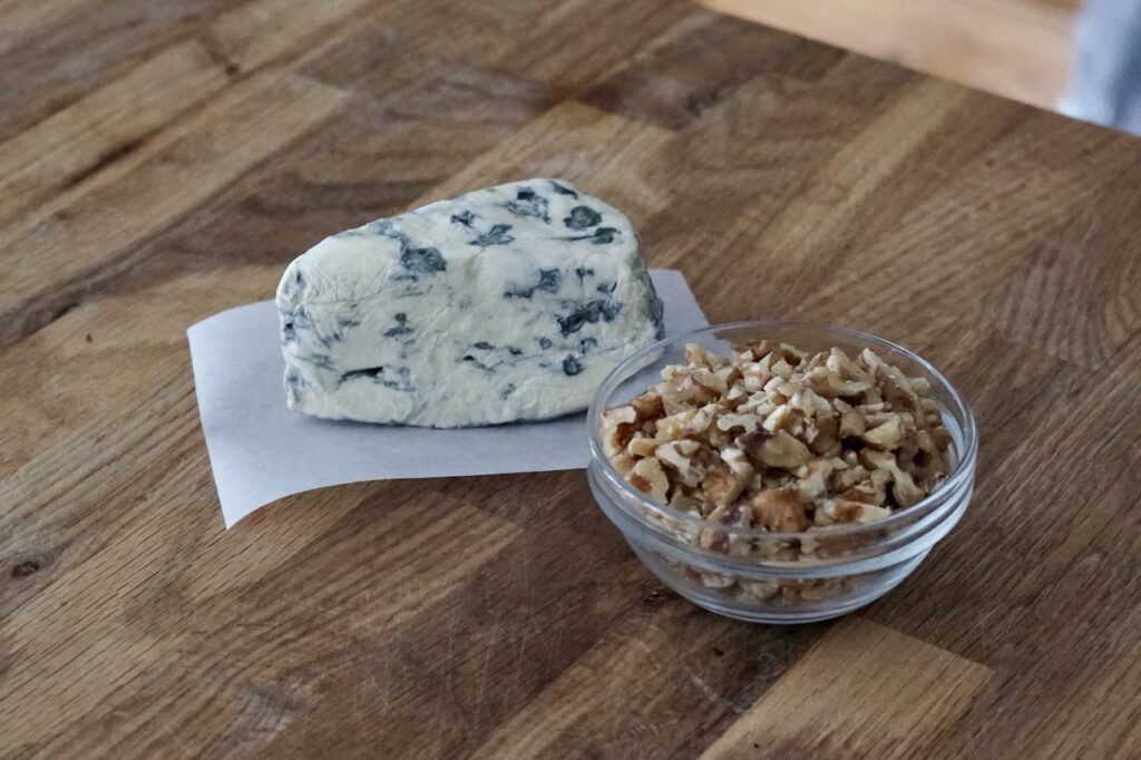 A wedge of Saint Agur blue cheese and a bowl of chopped walnuts.