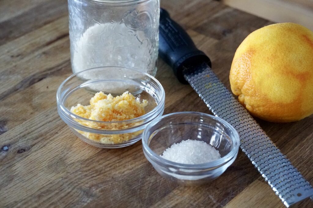 A jar of sanding sugar, a bowl of granulated sugar and a small bowl of orange zest.