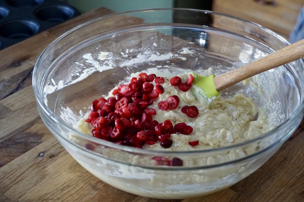 A bowl of the muffin batter with all of the sliced cranberries spilled on top.