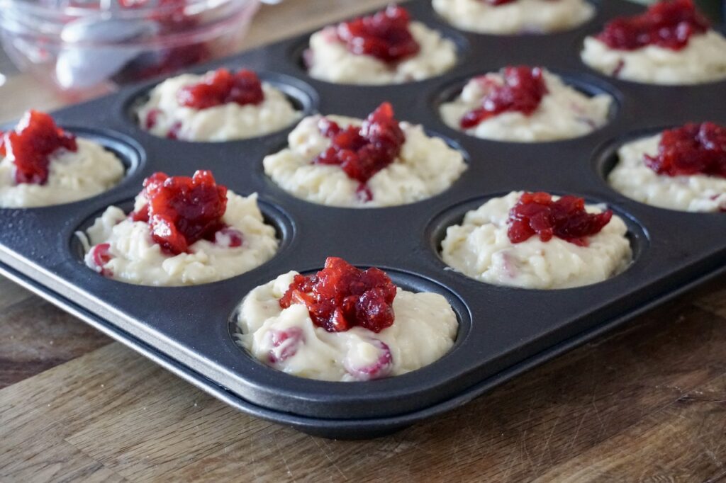 A muffin tray filled with the muffin batter plus a dollop of cranberry compote on each muffin.