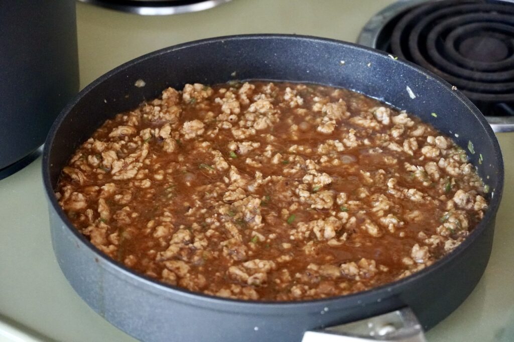 A large skillet filled with the simmering Chinese meat sauce.