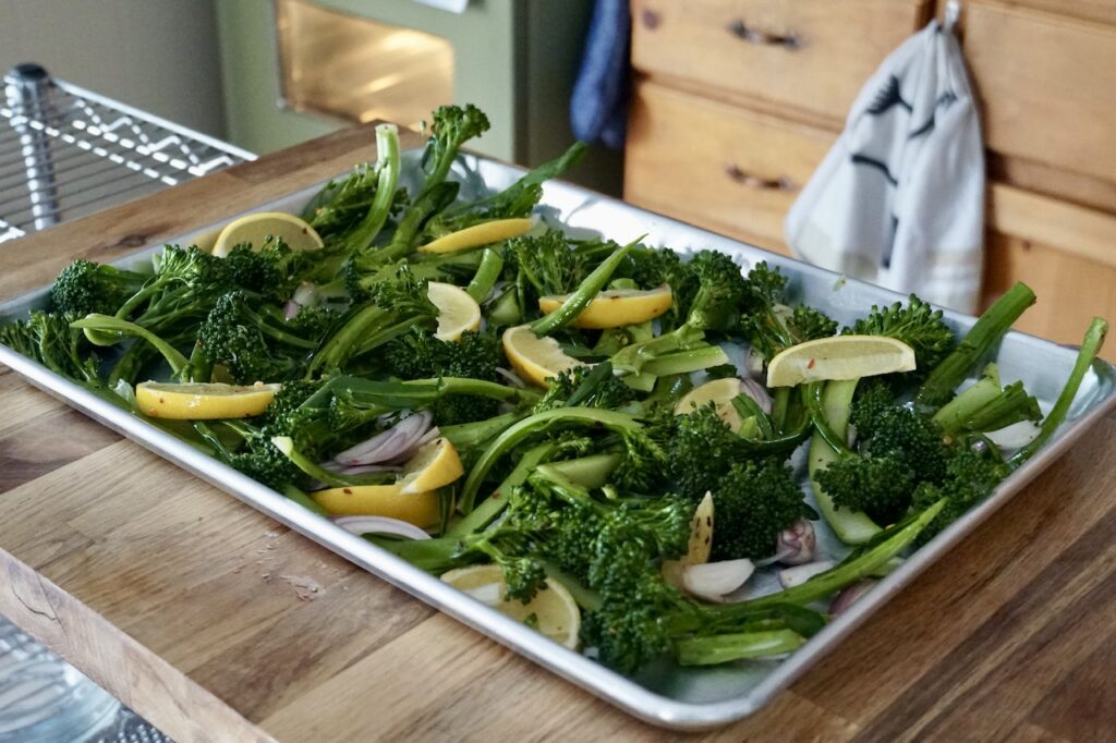 The broccolini, lemon and shallots spread out on a large baking tray.