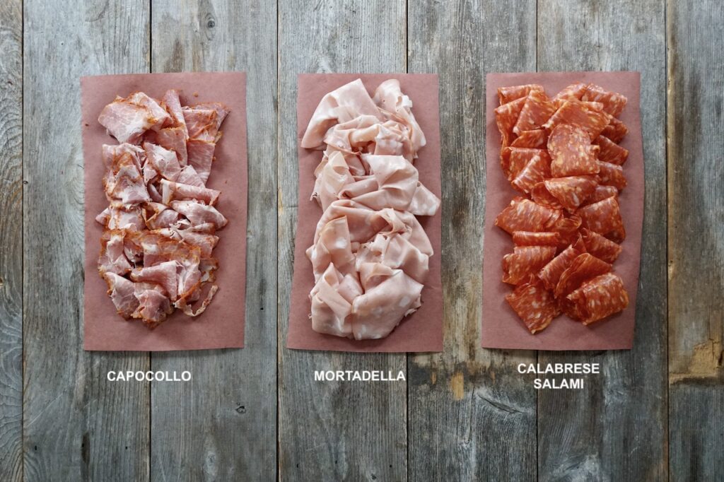 Three portions of Italian deli meats including: capocollo, mortadella and calabrese salami.
