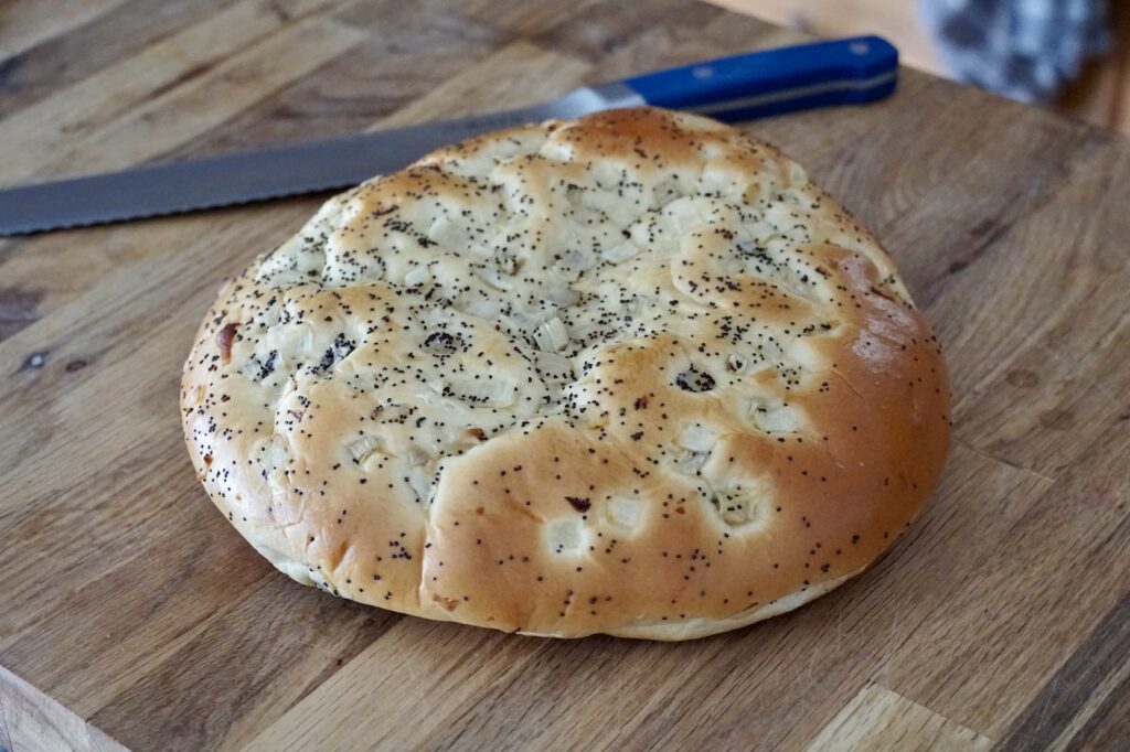 A large loaf of circular focaccia bread with an onion topping.