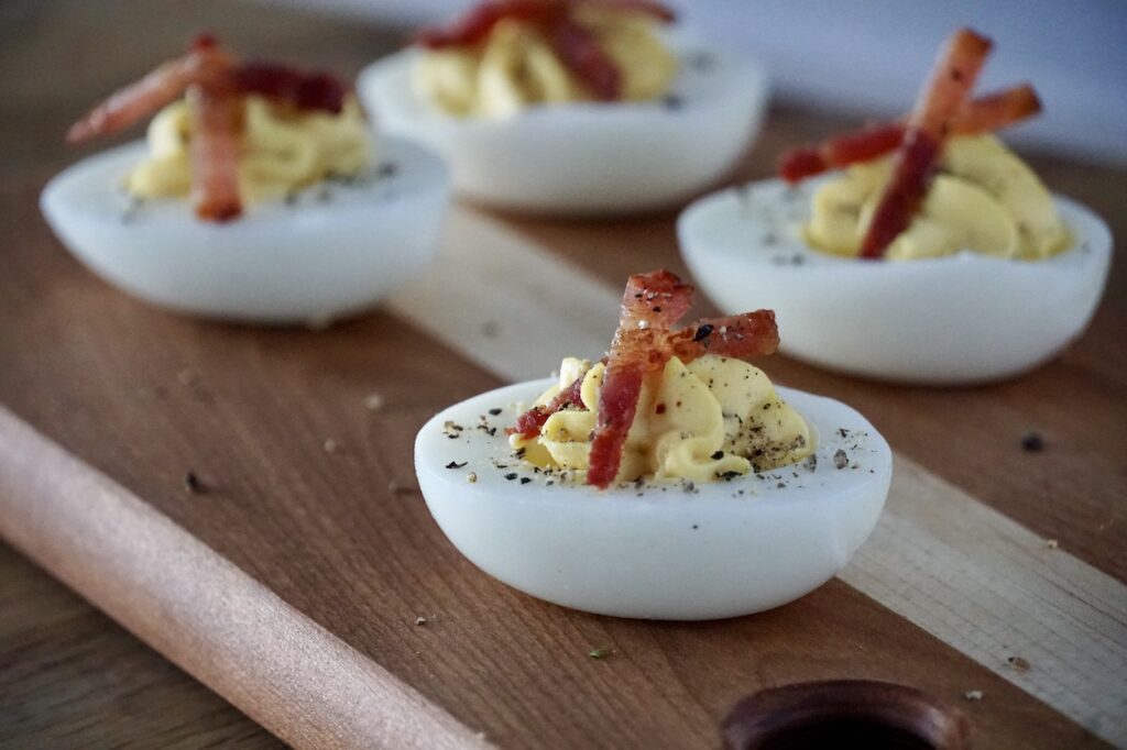 A deviled egg garnished with bacon and black pepper.