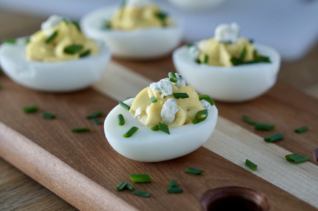 A deviled egg garnished with blue cheese and chopped chives.