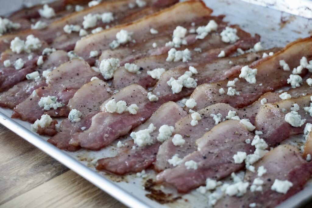 The bacon partially cooked topped with crumbled blue cheese and black pepper.