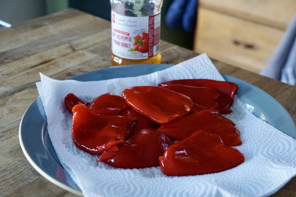Roasted red peppers placed on a plate with paper towels to remove excess moisture.