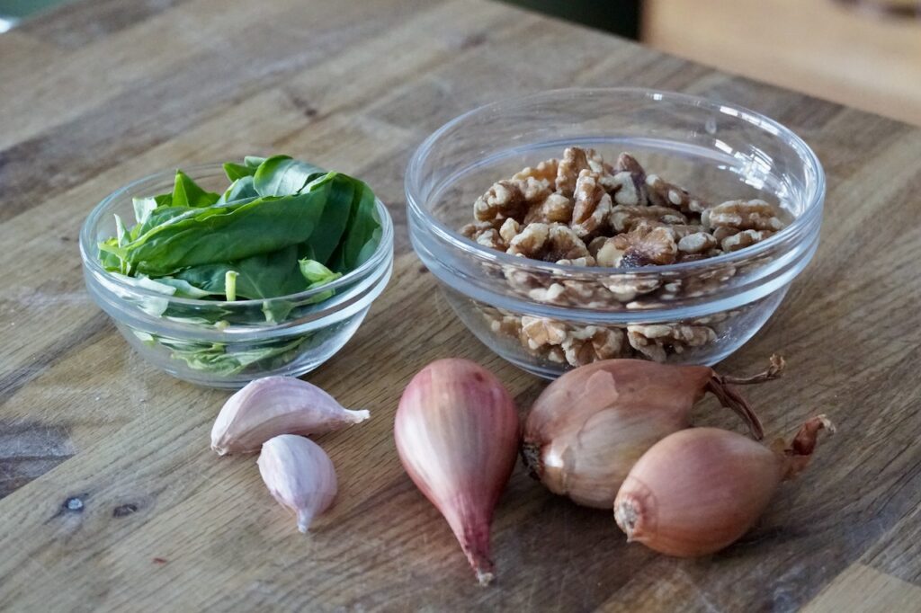 Fresh basil, a bowls of walnut halves, garlic and shallots.