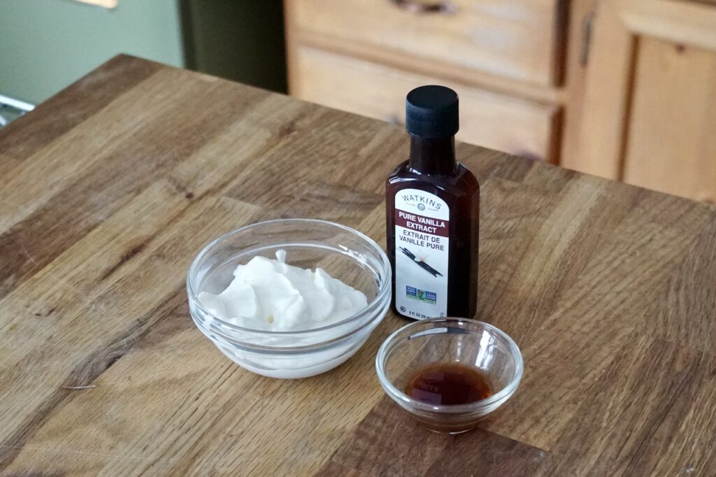 A bowl of sour cream and a small bowl of vanilla extract.