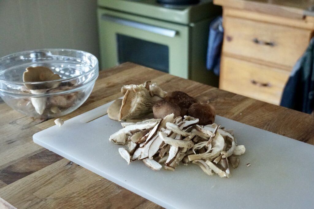 Thinly sliced shiitake and oyster mushrooms, resting on a cutting board.