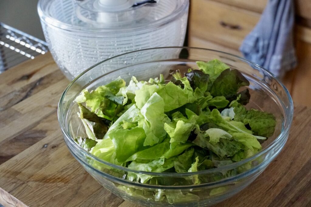 The three salad greens washed, sitting in a large glass bowl.