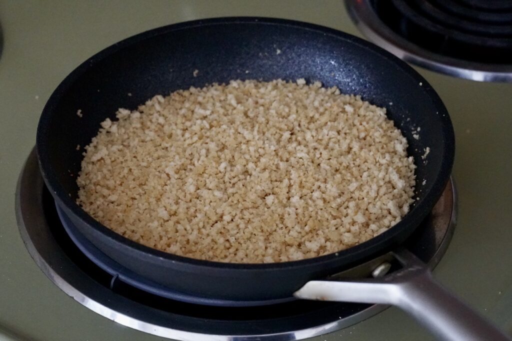 A skillet with the panko crumbs cooking on stovetop.