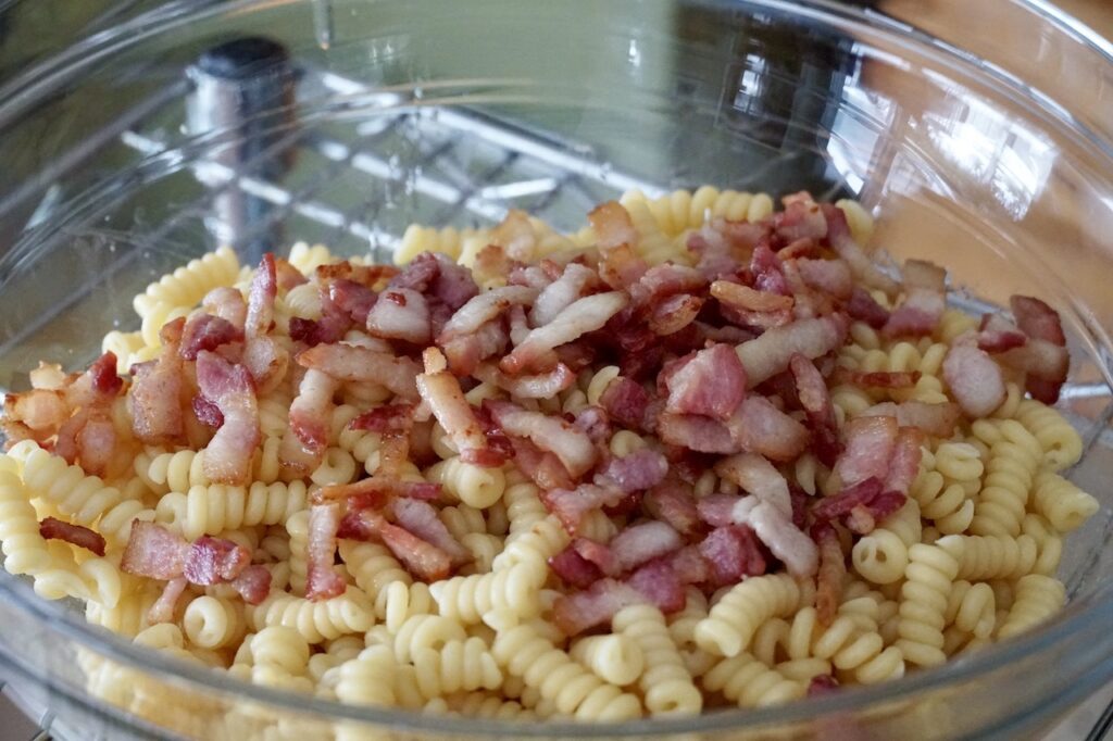 The pasta in a big bowl topped with the sautéed bacon.