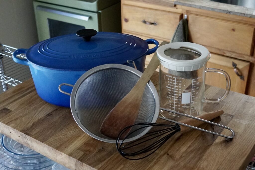A Dutch oven, strainer, wooden spoon and gravy separator.