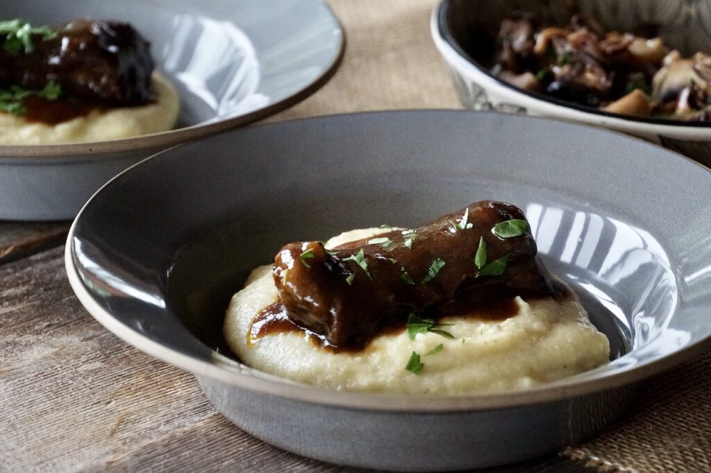 Braised Beef Short Ribs served on a healping of creamy polenta with Parmesan cheese.