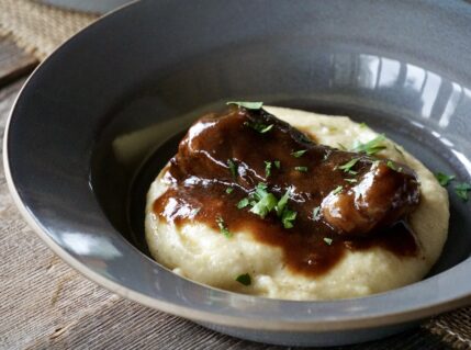 A bowl of the braised beef short ribs served on creamy polenta.