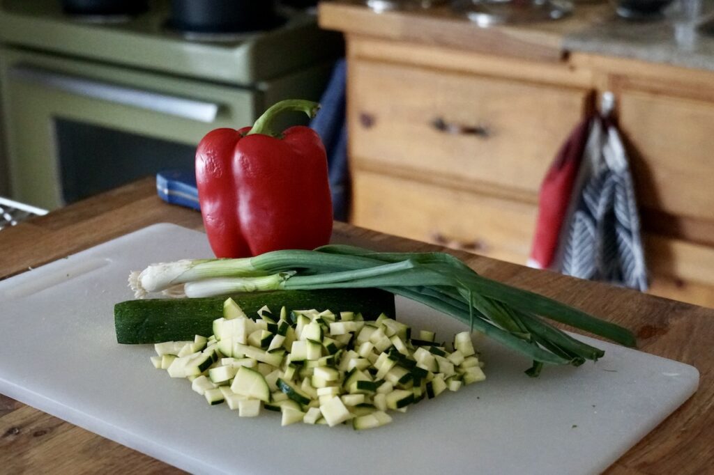 A red bell pepper, green onions and a mound of chopped zucchini.