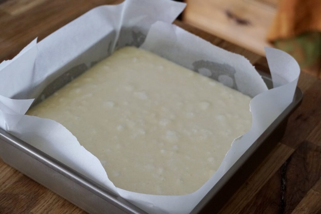 The Lemon Custard Cake poured into a prepared square pan, lined with parchment.