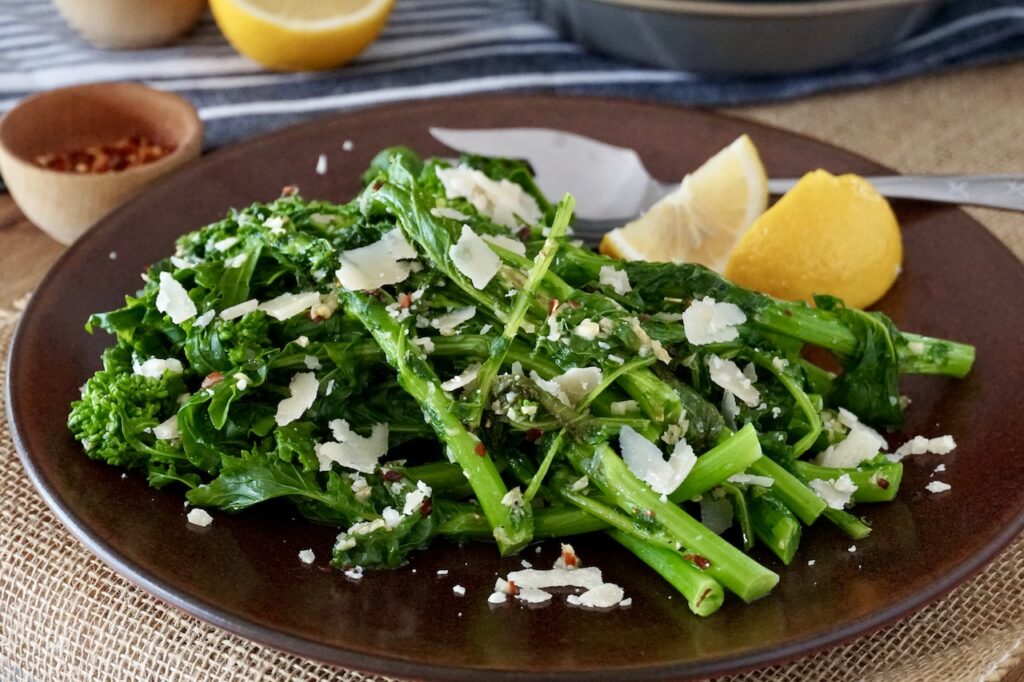 Rapini with garlic and Parmesan cheese served on a plate with lemon wedges.