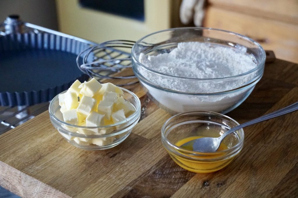 A classic tart crust recipe made with butter, a dry mix and an egg yolk all assembled beforehand in bowls.