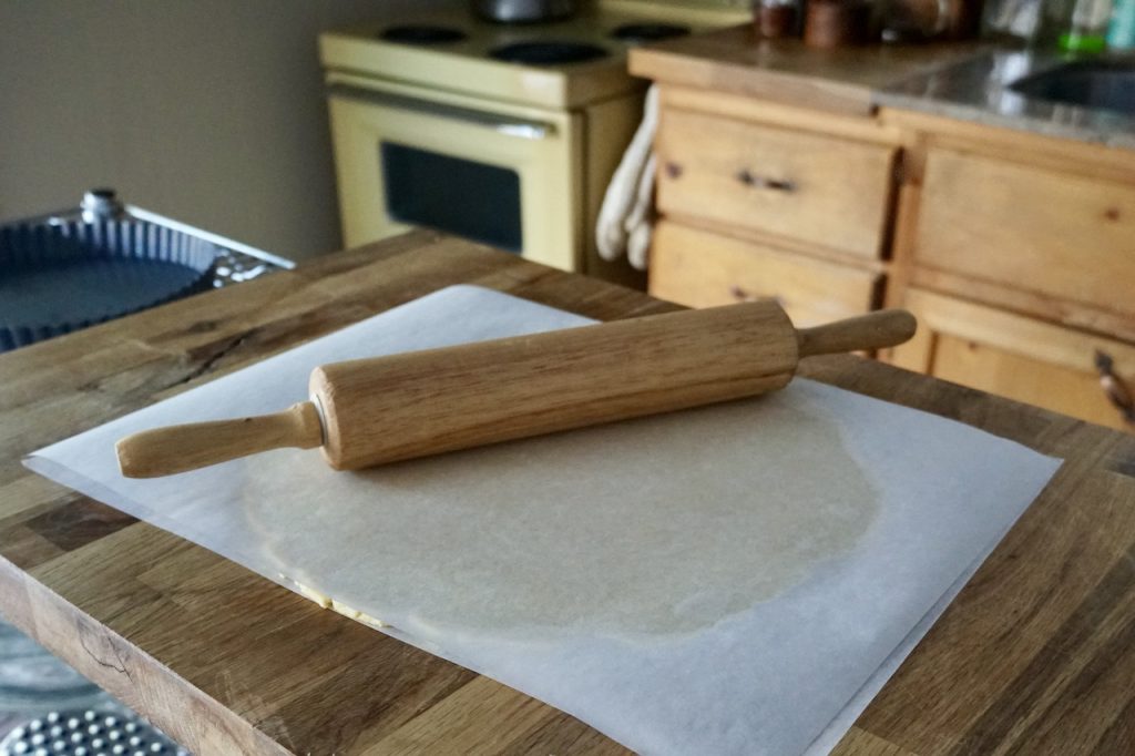 The disc of pastry dough rolled out flay between two pieces of parchment paper.