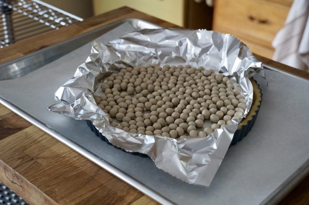 A tart shell covered with foil and weighted down with clay pie weights.