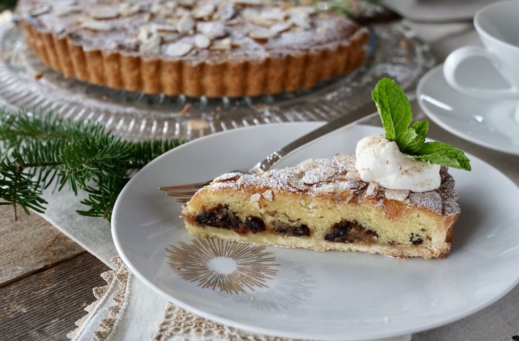 A wedge of Mincemeat Frangipane Tart served on a dessert plate with whipped cream.