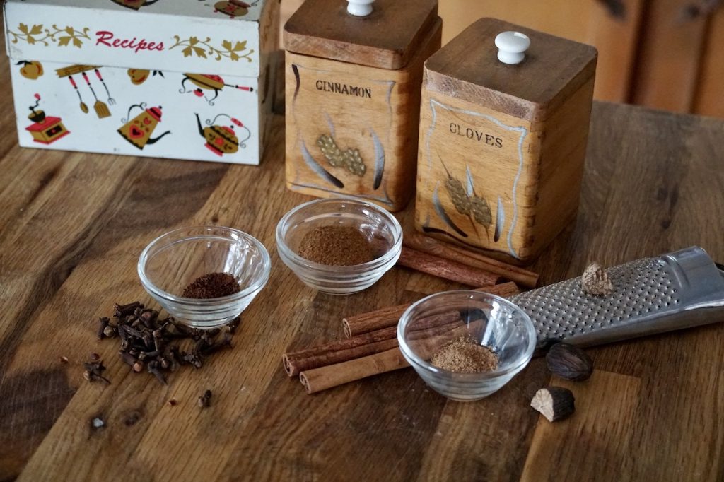 Assorted spices assembled in small bowls include: ground cloves, cinnamon and nutmeg.