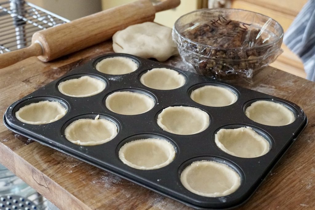 The rounds of pastry pushed down into the cups of the muffin tin.