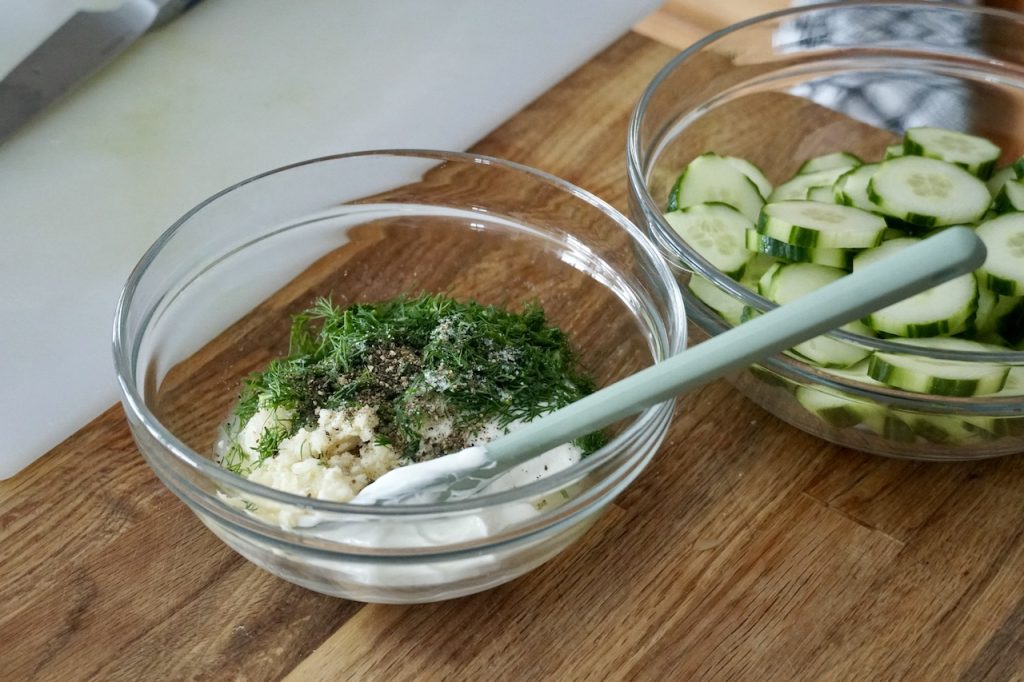 A bowl containing sour cream, garlic, lemon juice, fresh dill, sugar, salt and pepper.