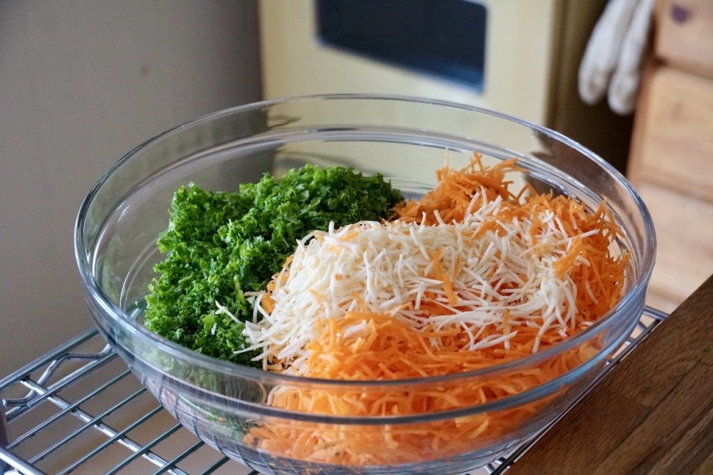 A large salad bowl filled with chopped kale and shredded carrots and parsnips.