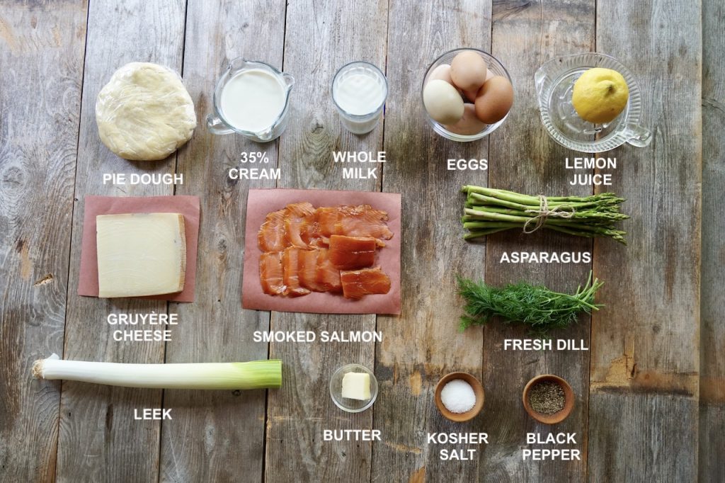 All of the ingrediens needed to make homemade Smoked Salmon Quiche including smoked salmon, eggs, Gruyère, asparagus, leeks and seasoning.