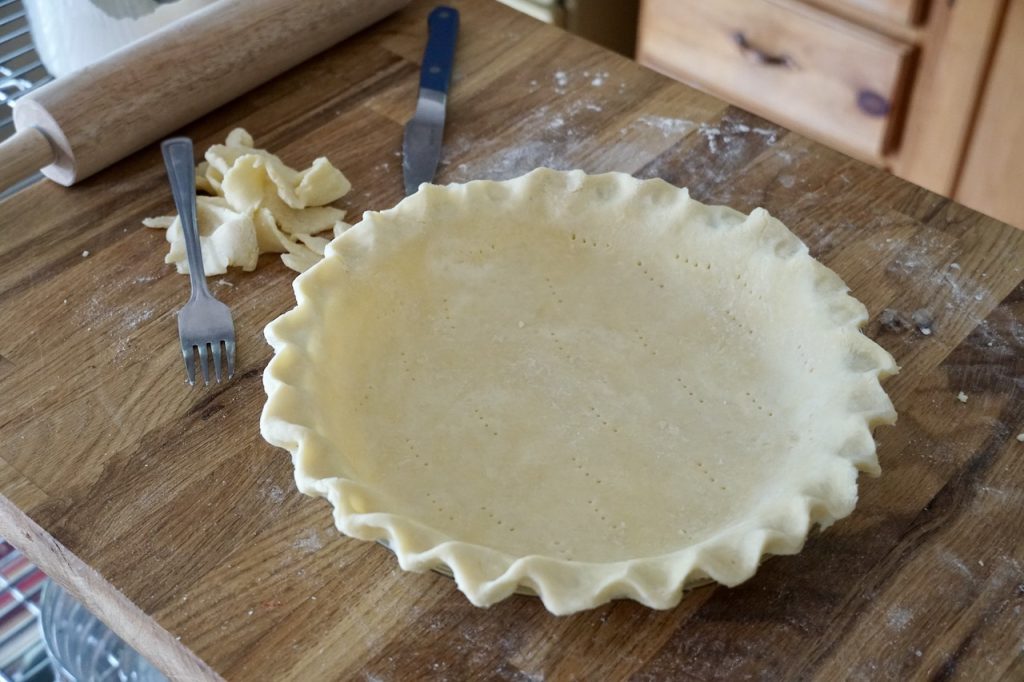 A pie plate filled with shaped all-butter pie dough.