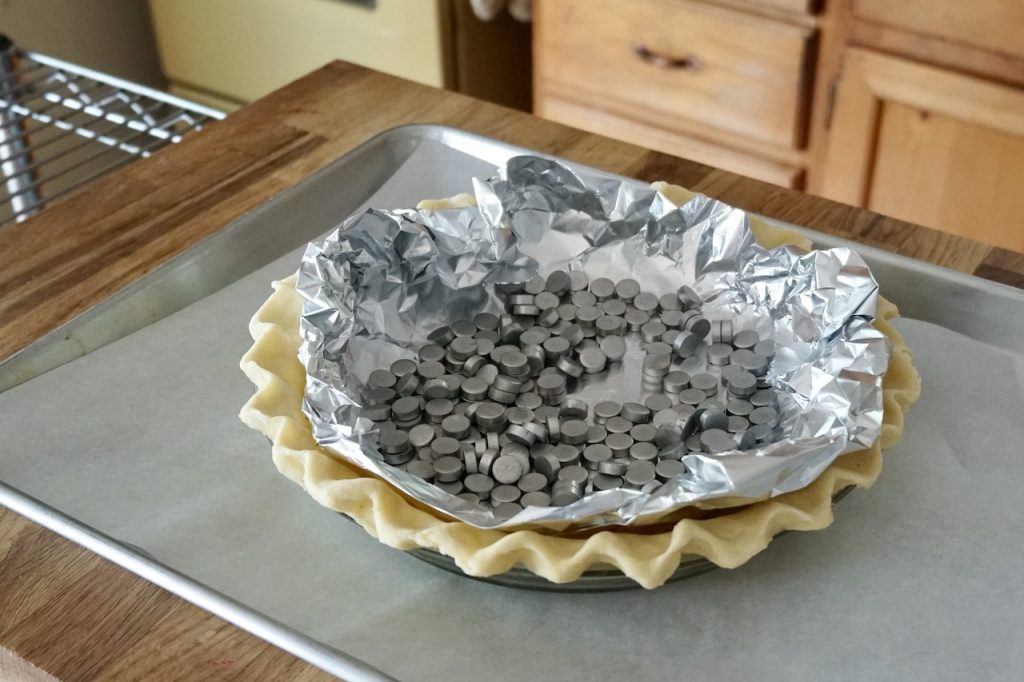The crust for the quiche topped with foil and pie weights, ready to be blind baked.