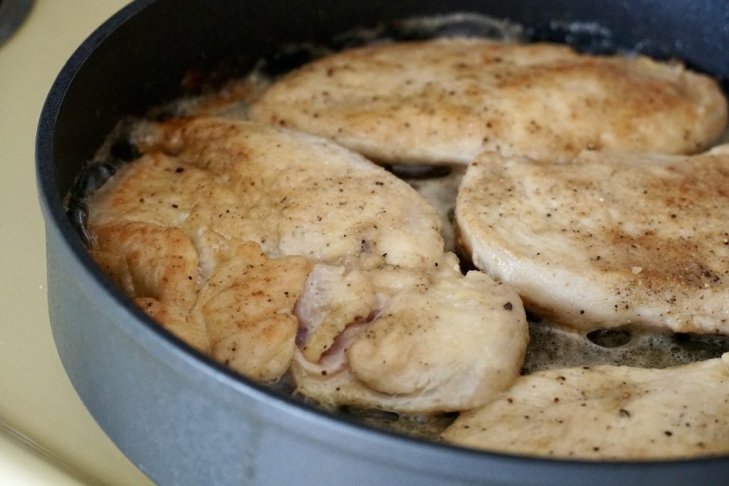 A large skillet containing the chicken breasts pan-fried in butter and oil.