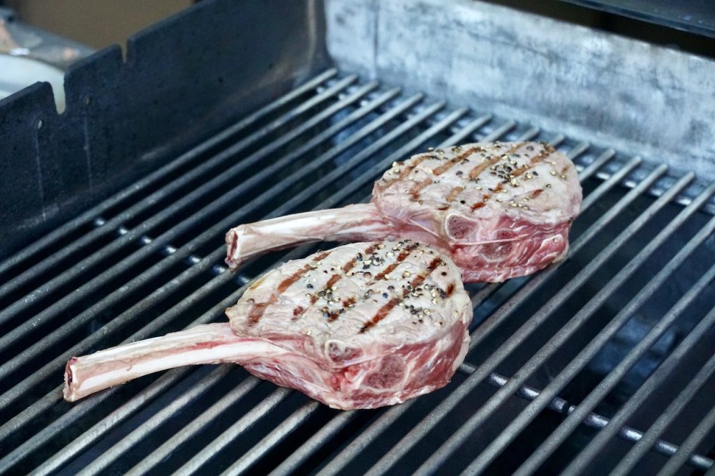 Two veal rib chops sitting on a grill over direct heat.