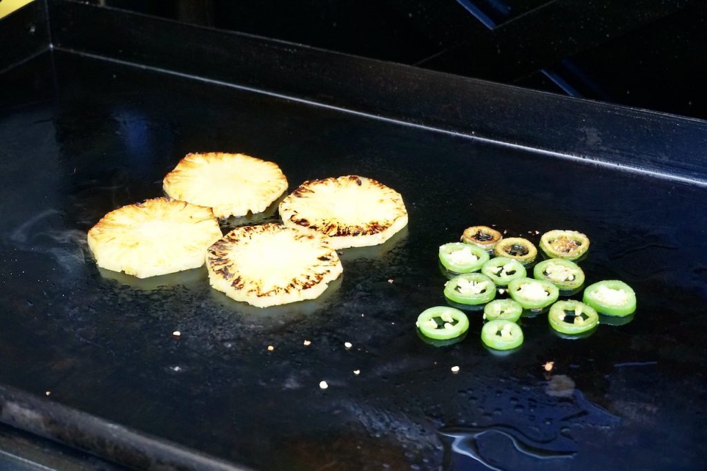 Slices of pineapple and jalapeño peppers cooking on the griddle.