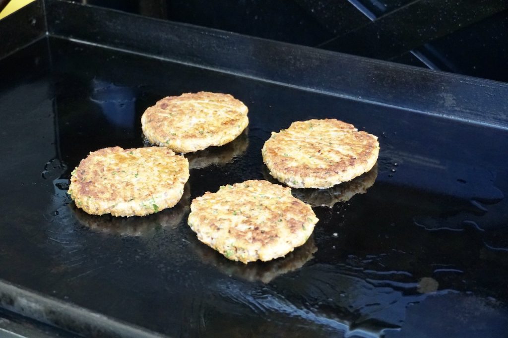 Tender, juicy chicken burger patties cooking on a flattop griddle.