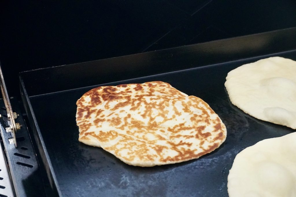 Flatbreads cooking on a large, flat griddle.