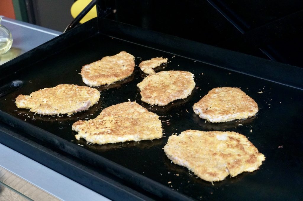 Breaded pork cutlets cooking on a flattop griddle.