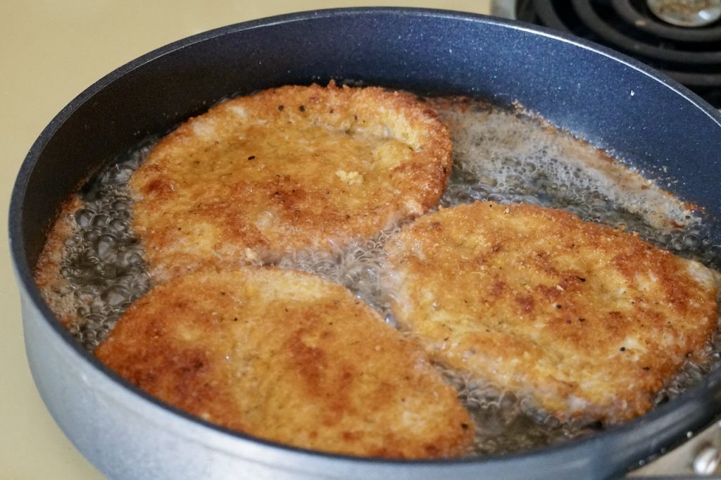 Crispy pork schnitzel cooking in a deep skillet.