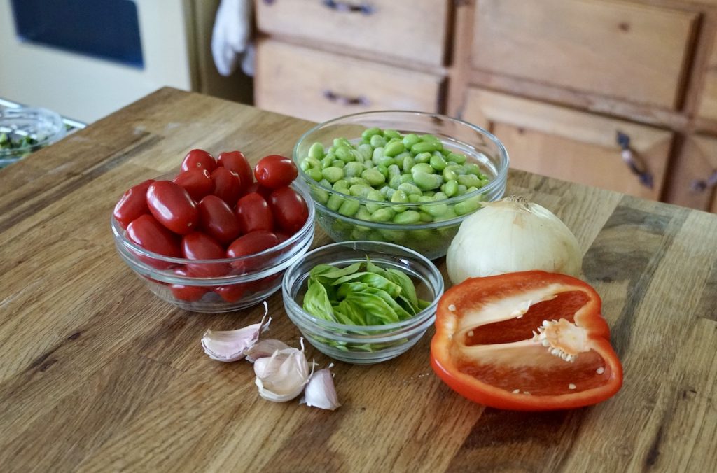 Bowls of fresh vegetables including tomatoes, red pepper, fresh herbs plus onion, garlic and edamame.